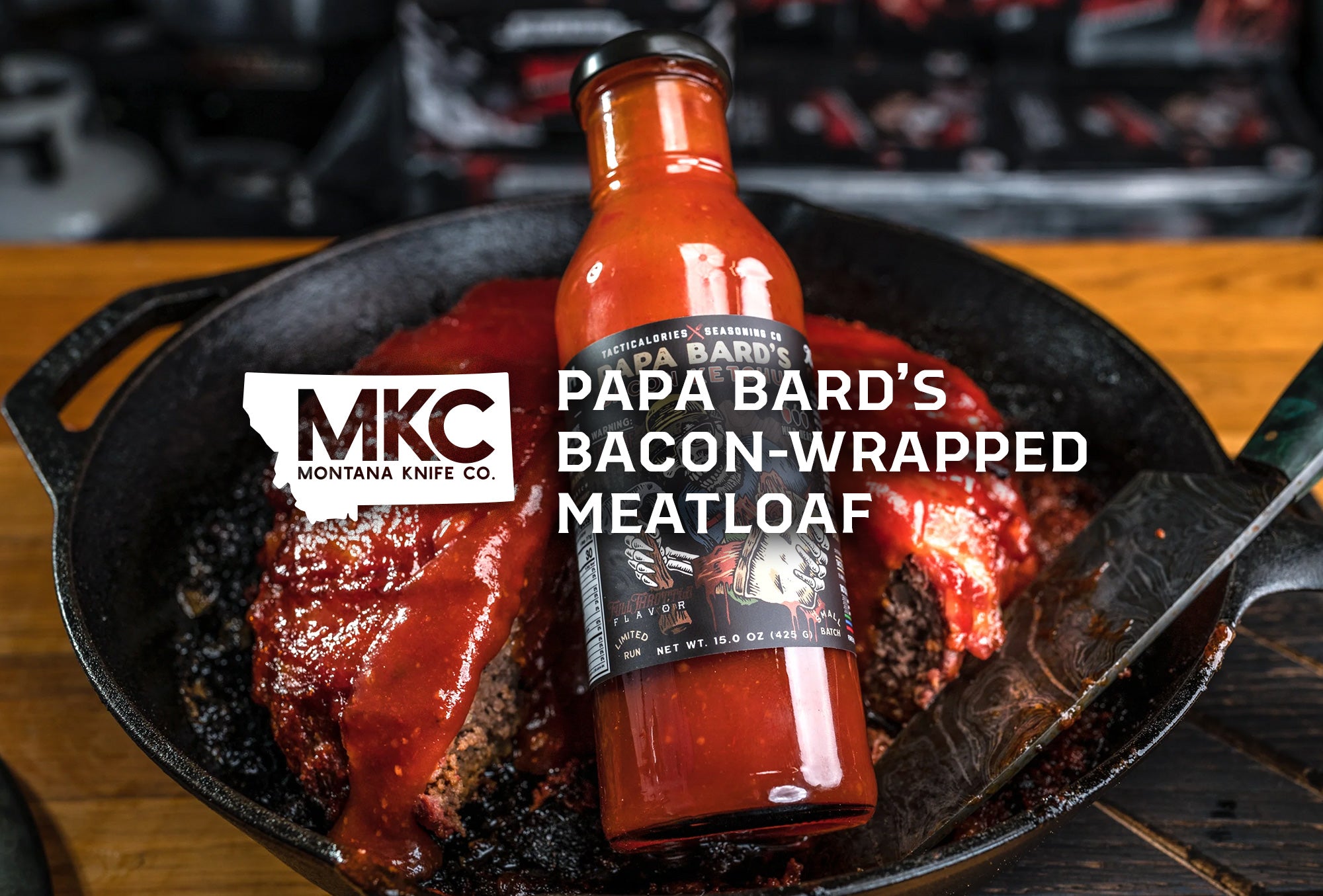 A bottle of Papa Bard's Bacon Ketchup rests on a hunk of bacon-wrapped meatloaf in a cast iron skillet.