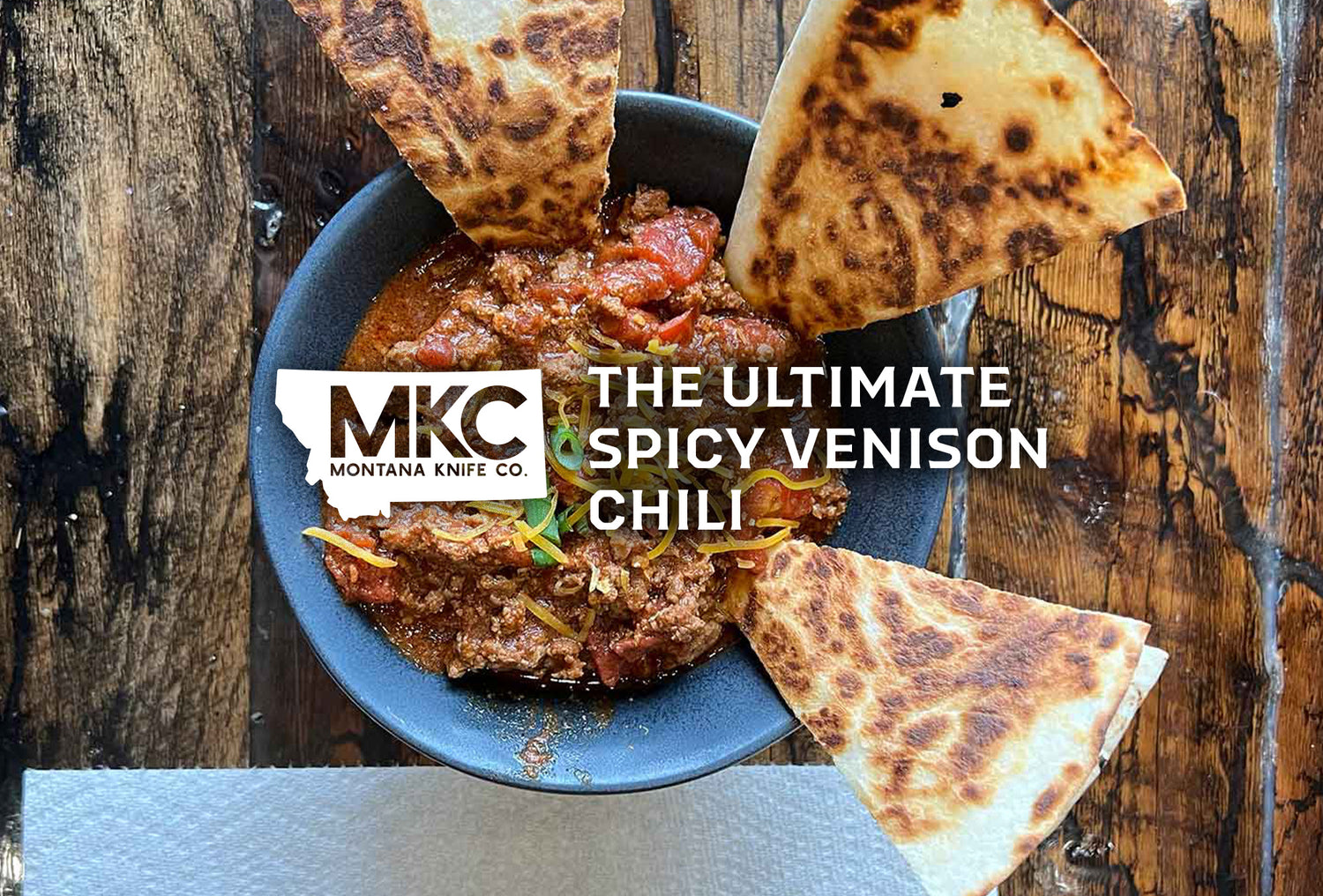 A stone bowl of delicious spicy venison chili rests on a rustic wooden dining table.