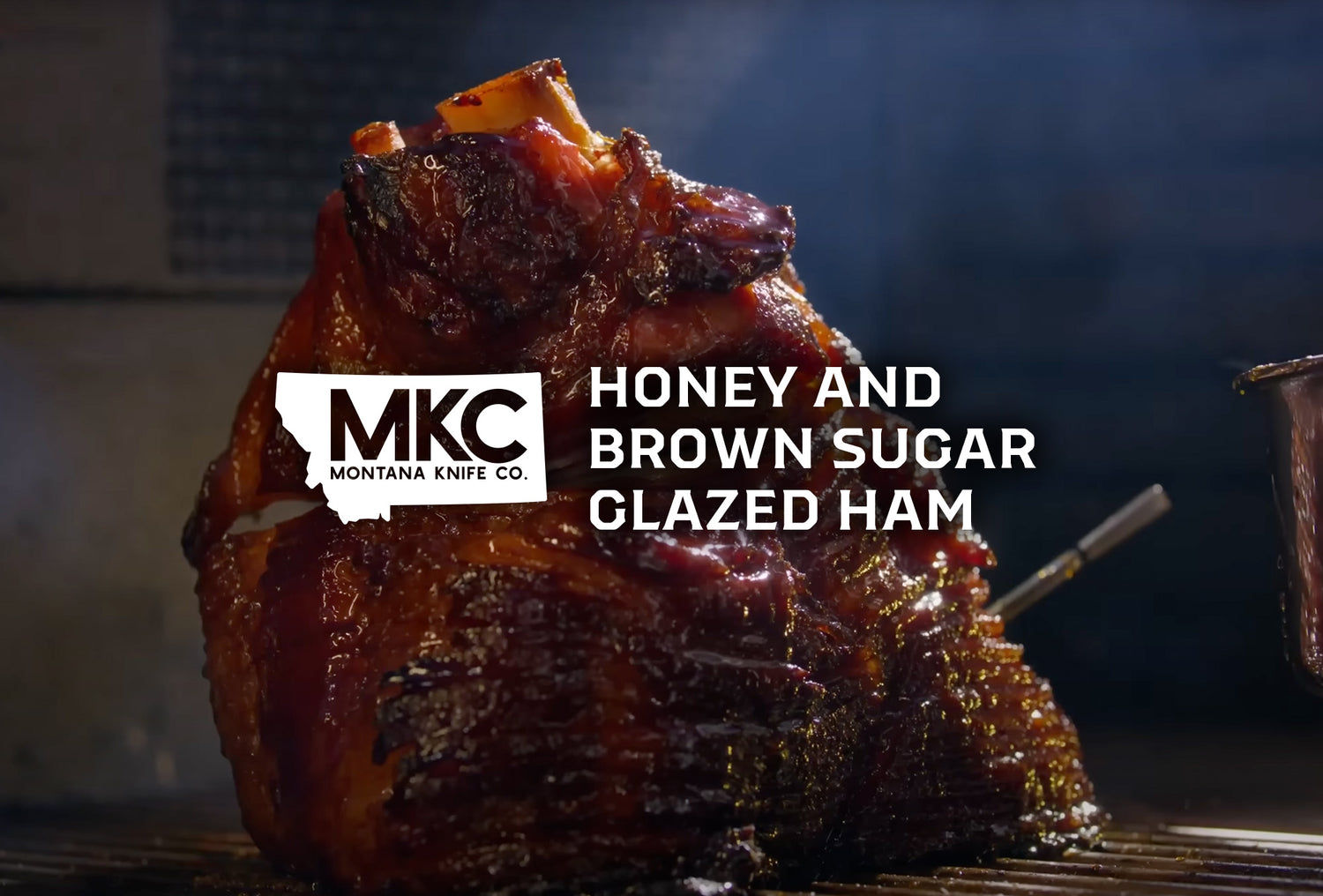 A large honey brown sugar glazed ham rests on iron grates of a smoker.