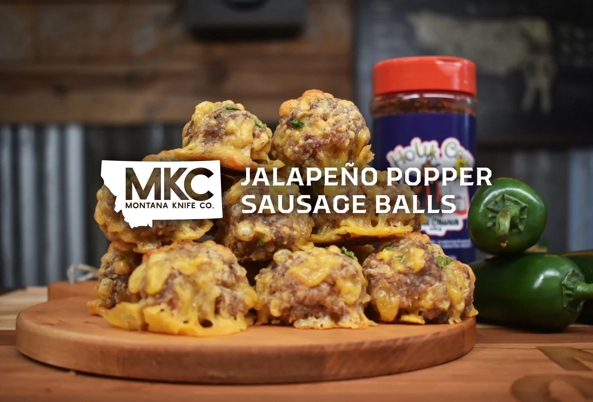 A jalapeno popper sausage balls topped with melted cheese on wooden board, with fresh jalapenos and seasoning jar.