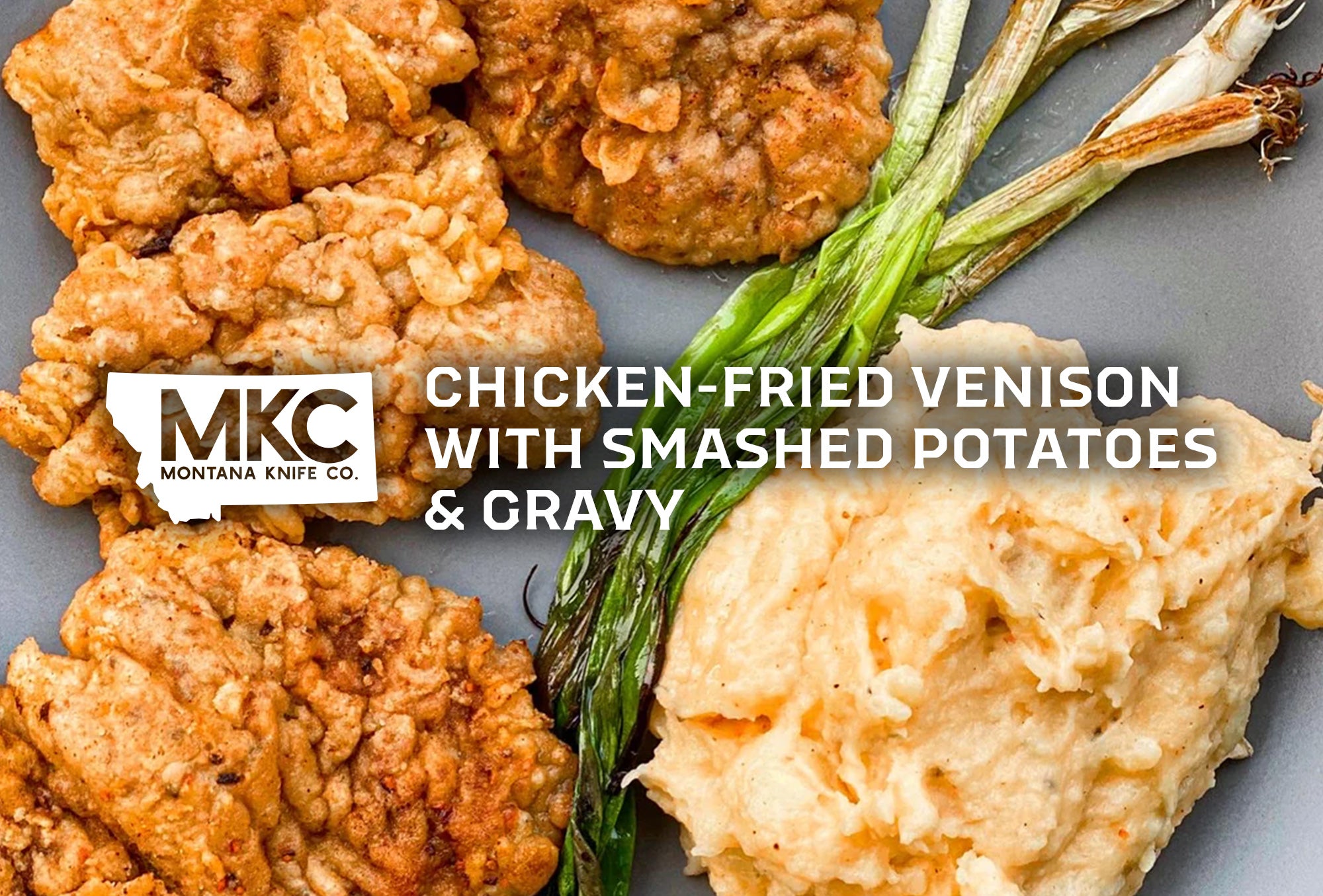 A plate of crispy, golden-brown chicken-fried venison served with creamy smashed potatoes and roasted green onions.