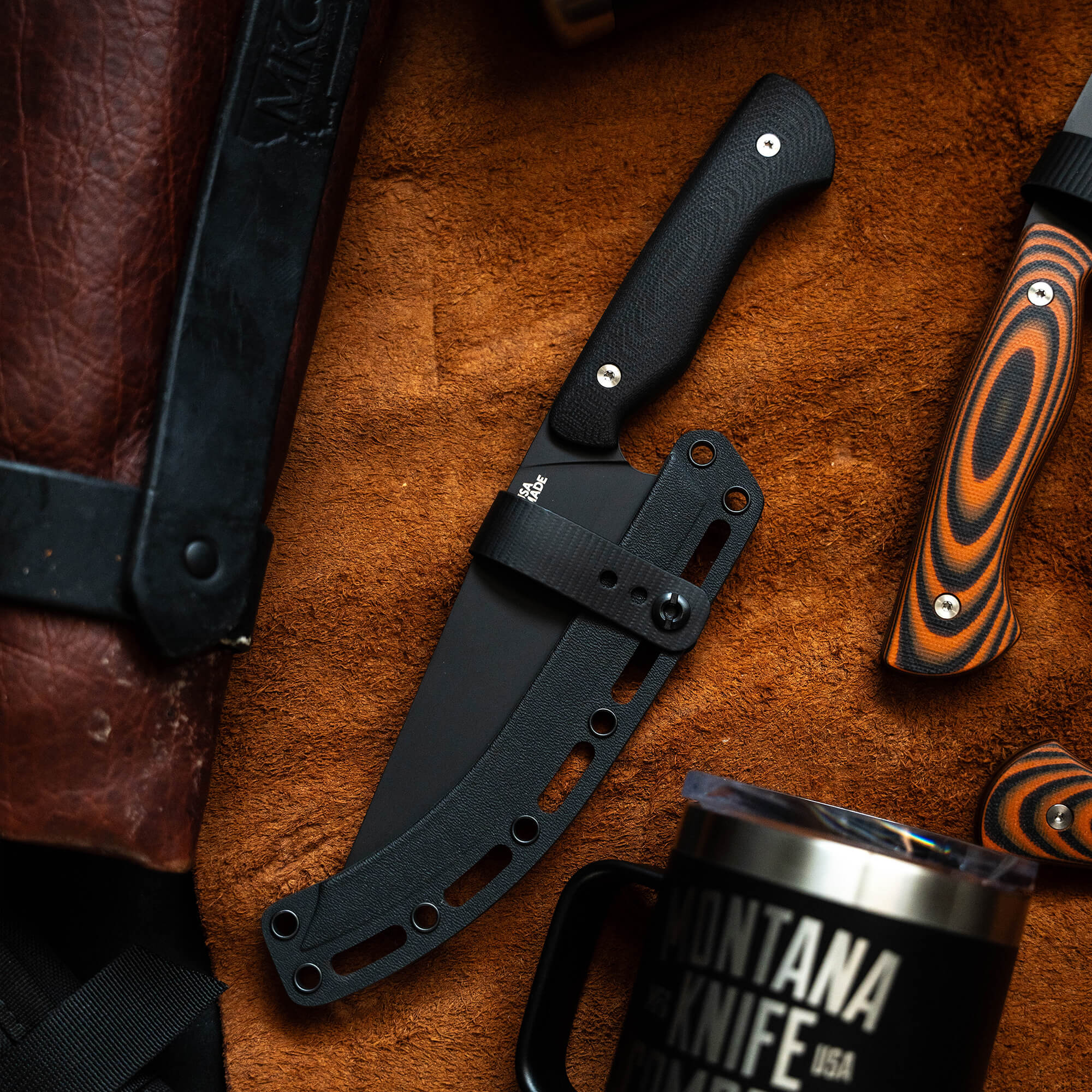 Alt text: A high-quality Meat Church chef knife with a black handle and sheath, displayed on a textured leather surface next to a leather knife case and a black mug with logo.