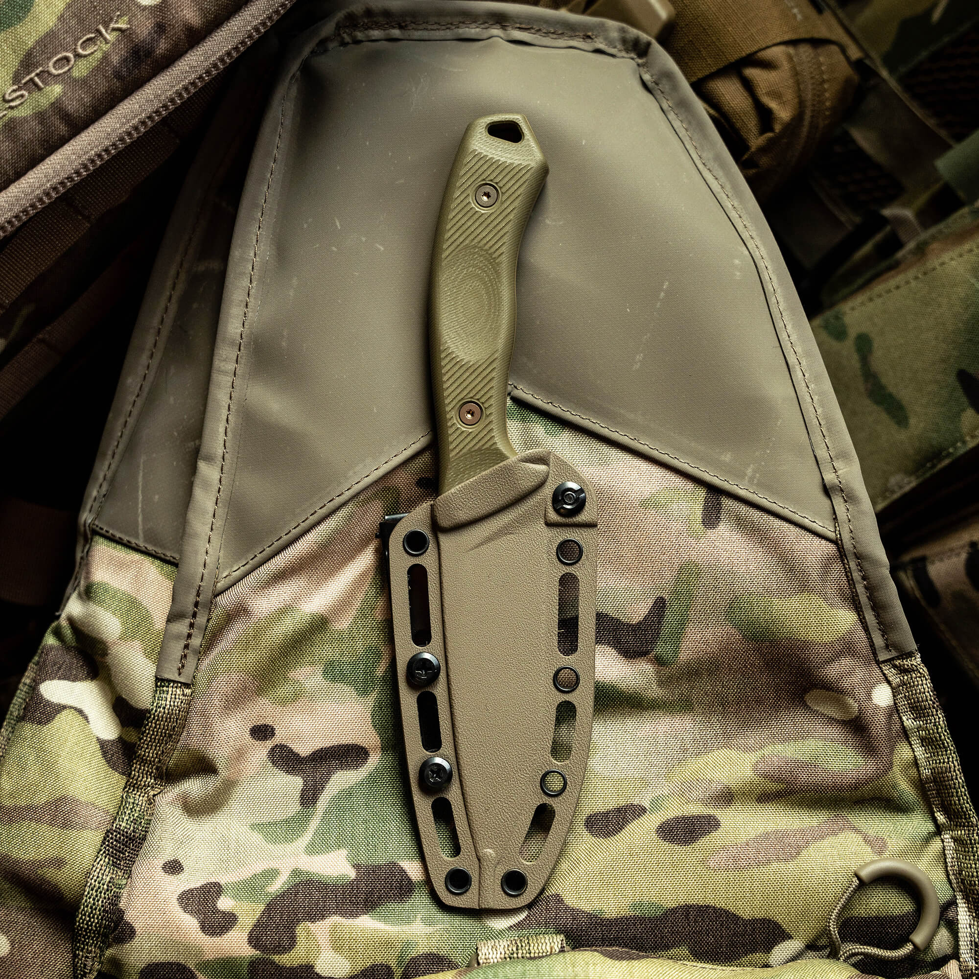 Alt text: "A coyote-colored TF24 Kydex sheath with a secured knife, attached to a camouflage patterned tactical backpack."